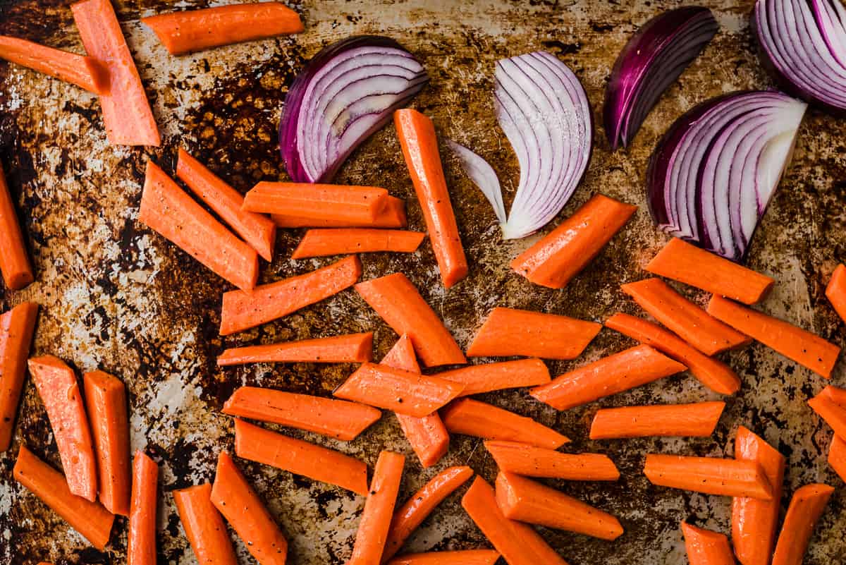 Carrots and onions on a baking sheet before being roasted.
