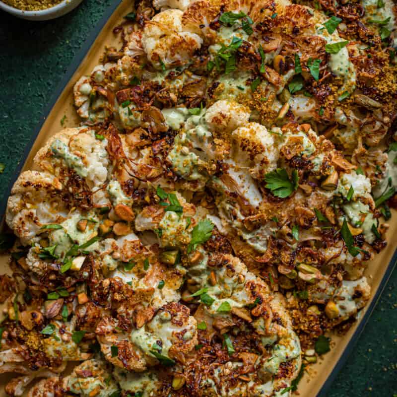roasted cauliflower steaks with caramelized shallots and tahini sauce on yellow tray