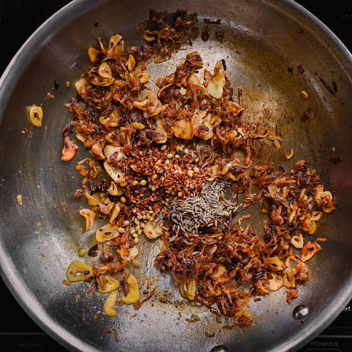cumin and coriander seeds and chili flakes with caramelized shallots and garlic in skillet