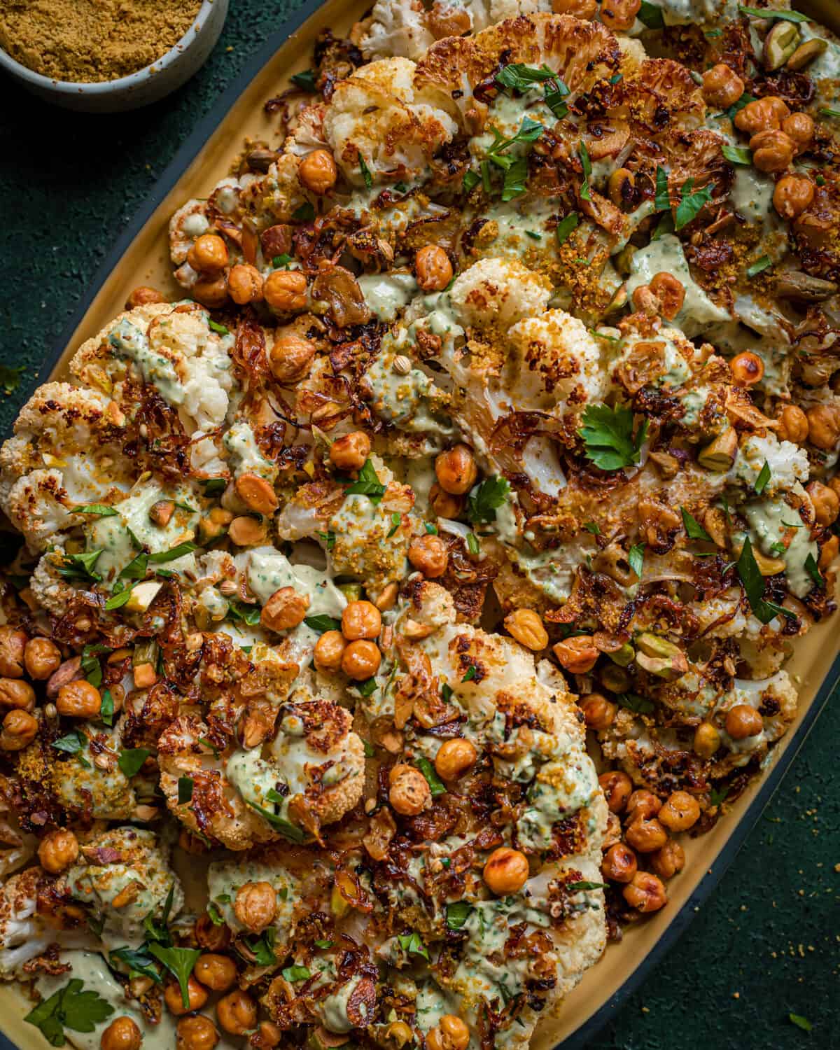 roasted cauliflower steaks and chickpeas with caramelized shallots and tahini sauce on yellow tray