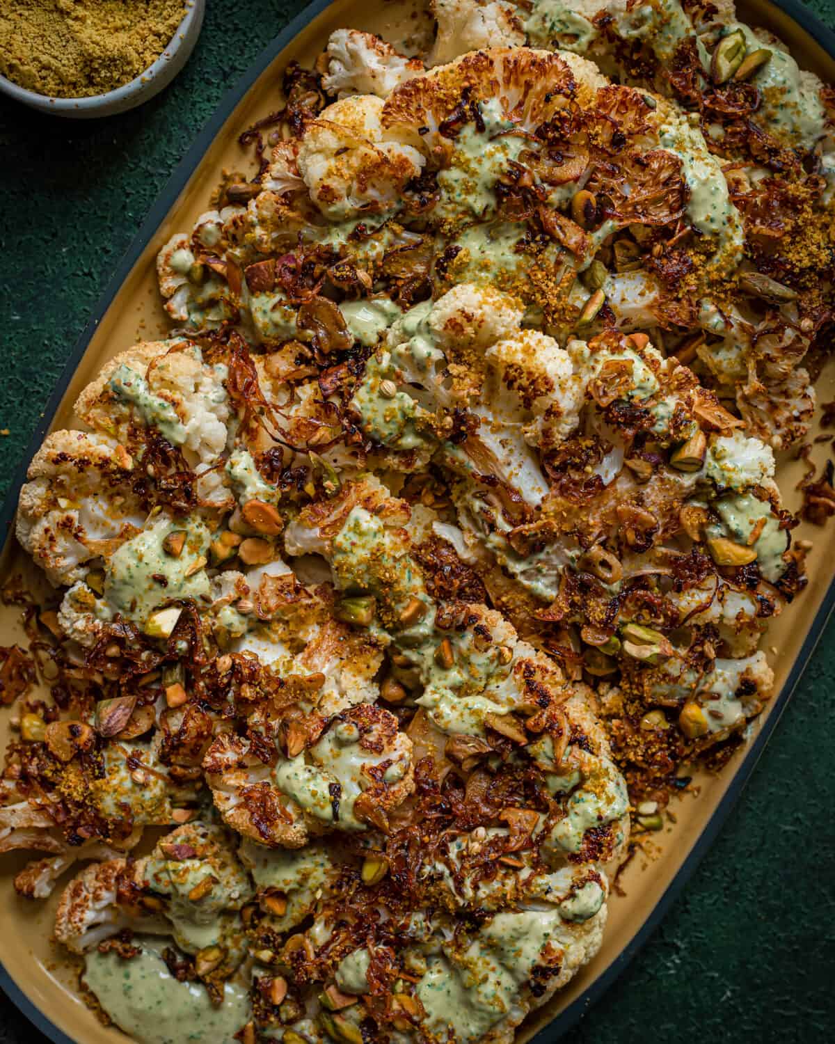 roasted cauliflower steaks with caramelized shallots and tahini sauce on yellow tray