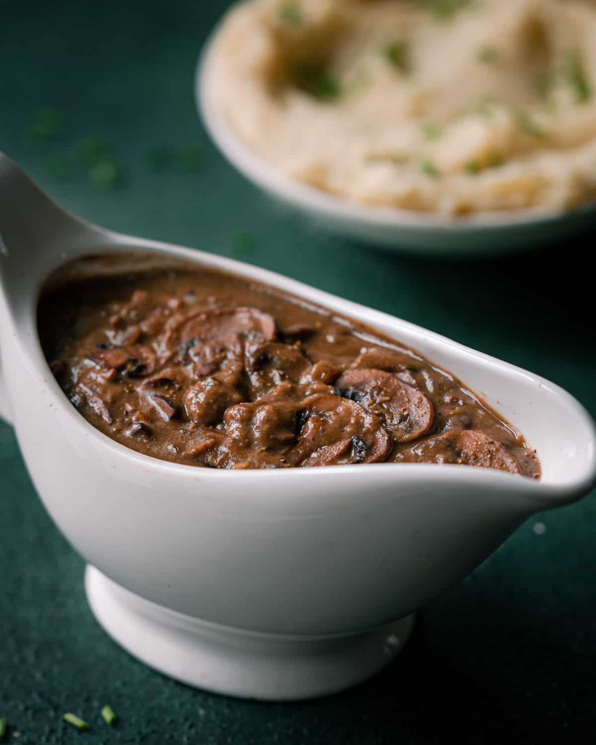 vegan gravy with mushrooms in a gravy boat with mashed potatoes in the background