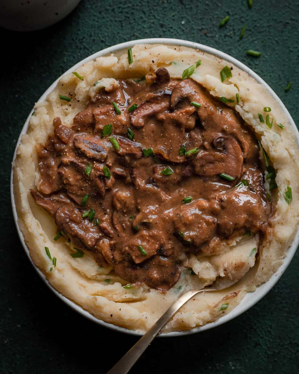vegan gravy with mushrooms on top of bowl of mashed potatoes on green background
