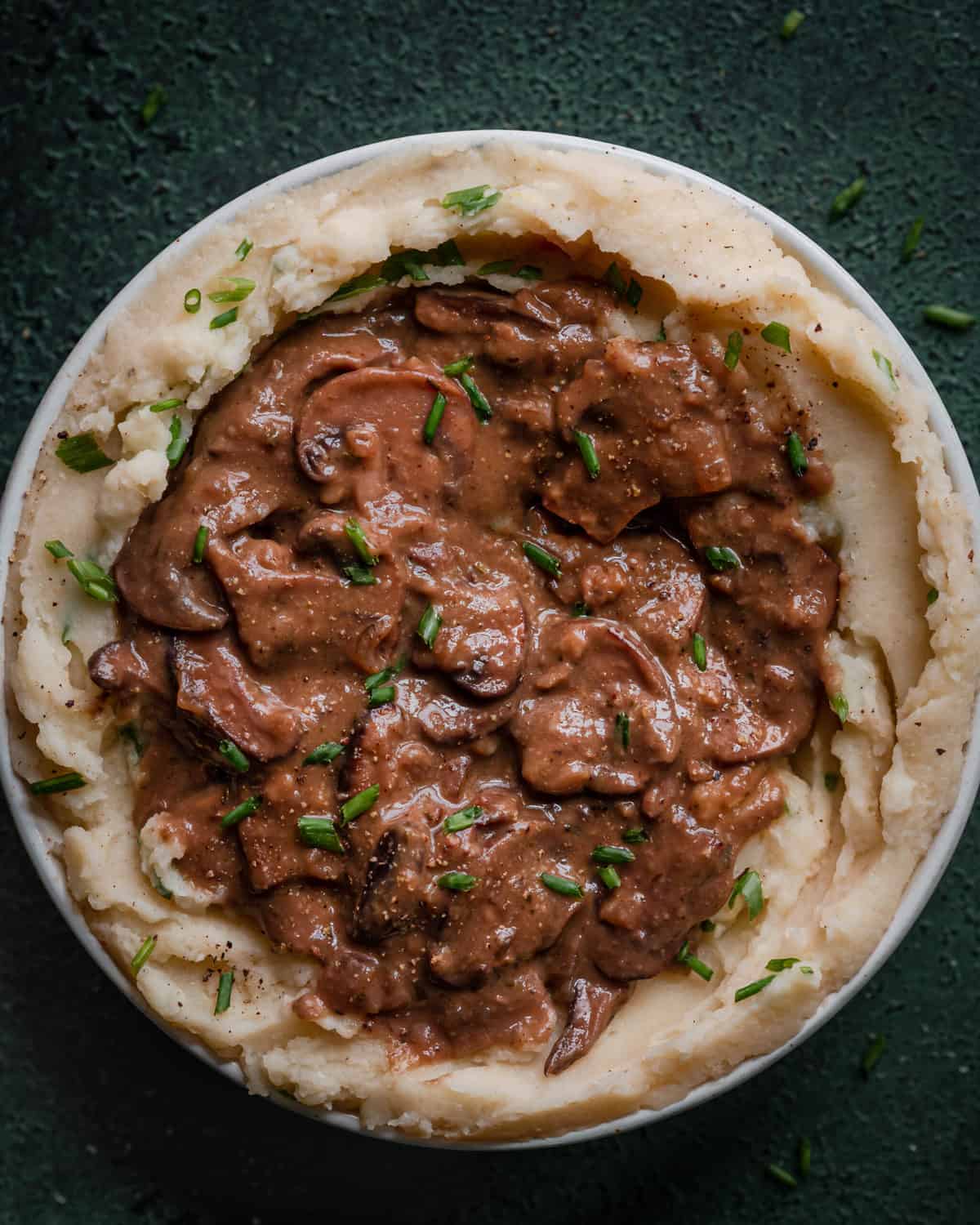 vegan gravy with mushrooms on top of bowl of mashed potatoes on green background