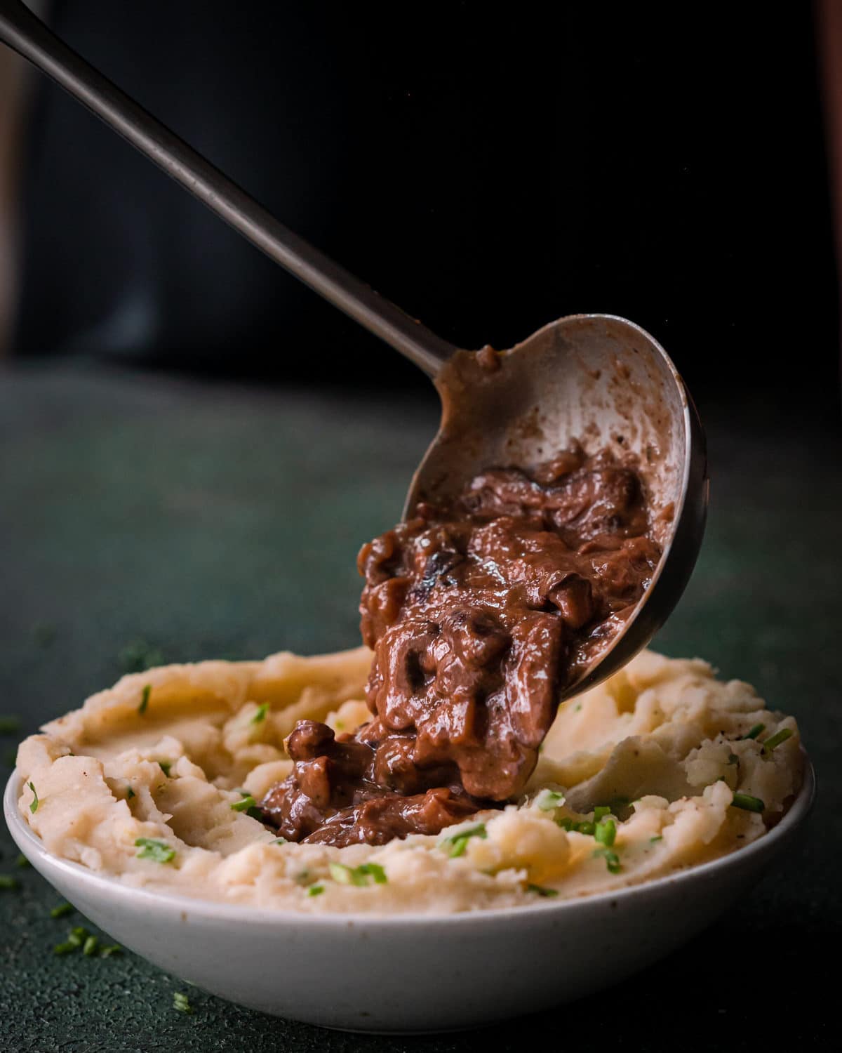 ladle spooning mushroom gravy onto mashed potatoes