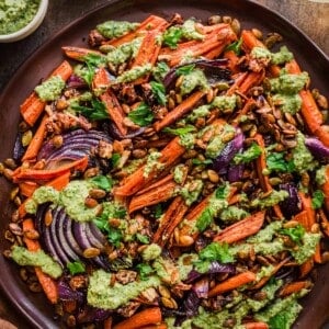 big plate of roasted carrots, red onions and dates covered in pesto.