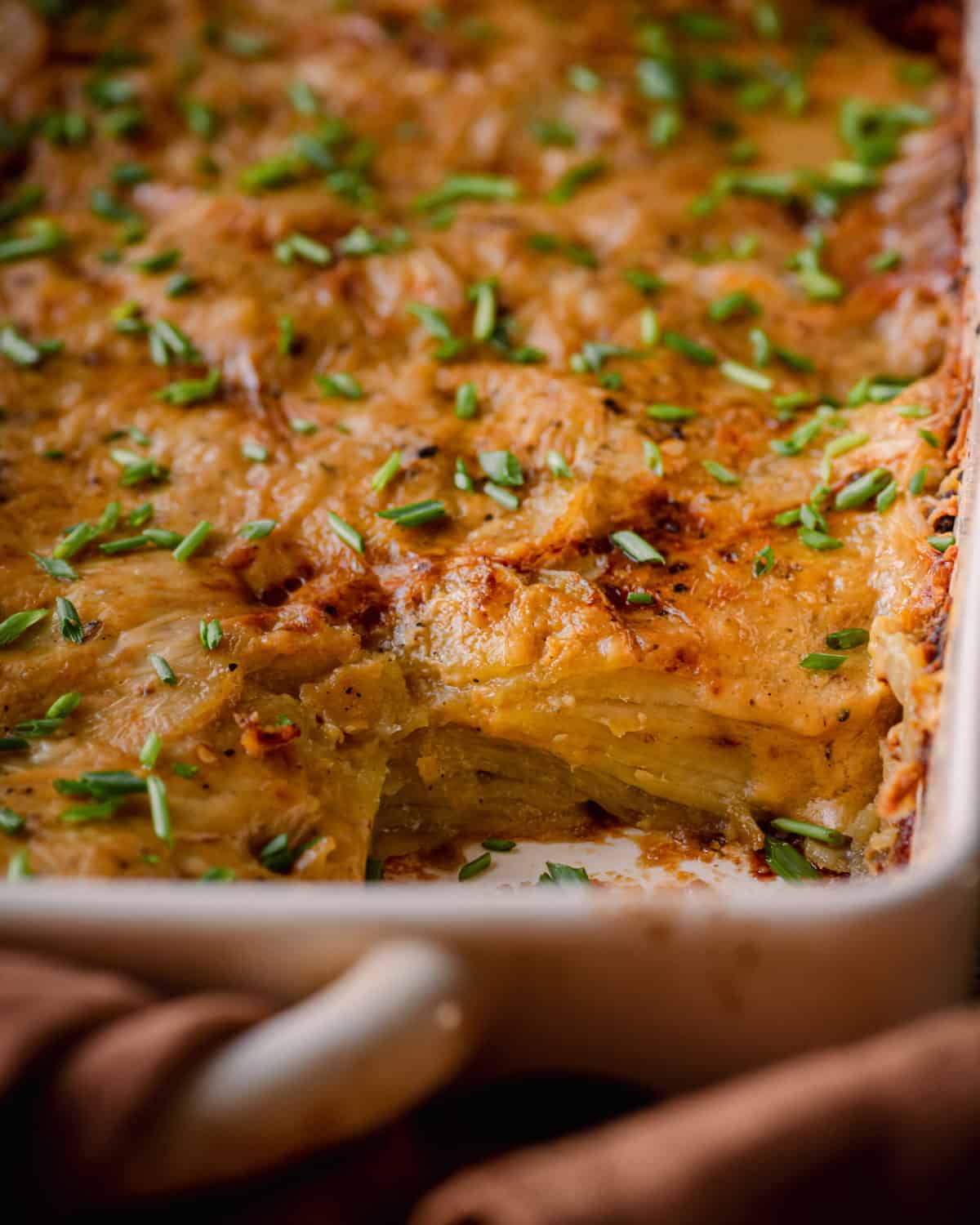closeup shot of cheesy vegan scalloped potatoes in casserole pan topped with chives