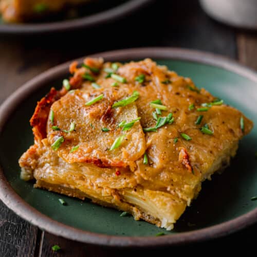 slice of vegan scalloped potatoes topped with chives on green plate.