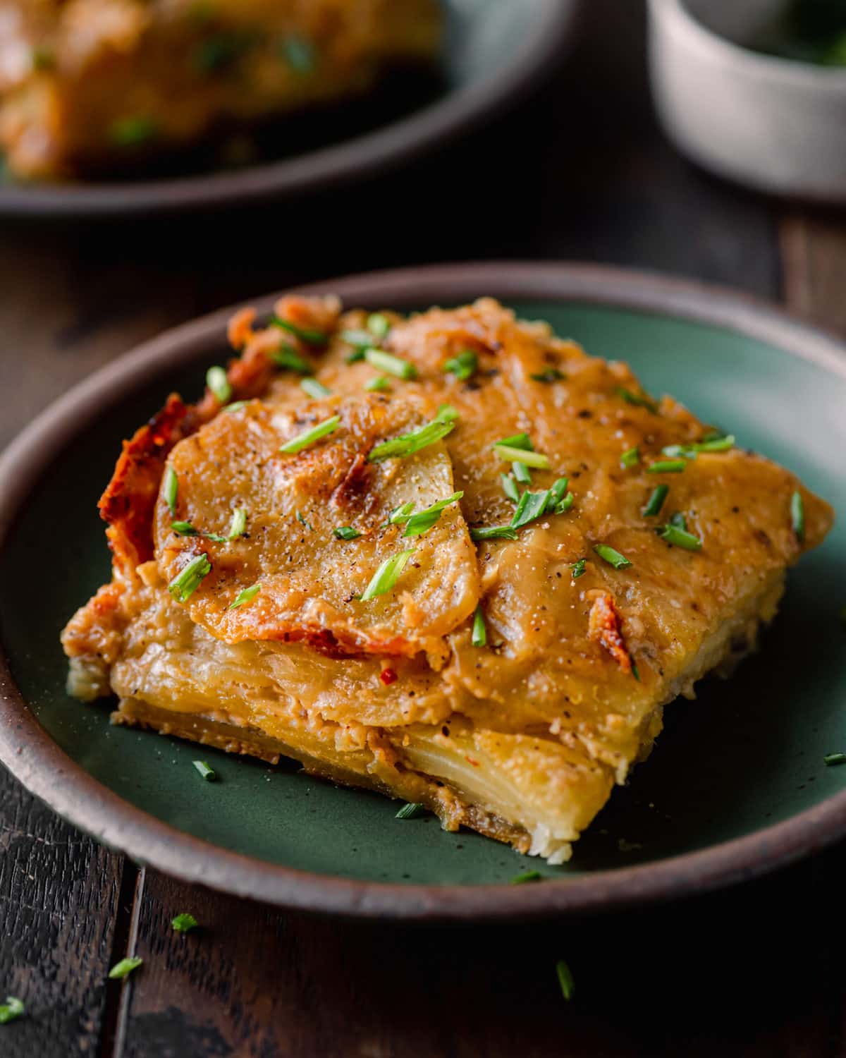 slice of vegan scalloped potatoes topped with chives on green plate