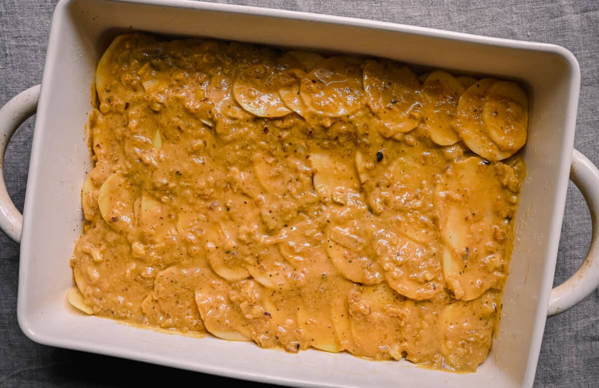 cheesy sauce spread out over potatoes for vegan scalloped potatoes