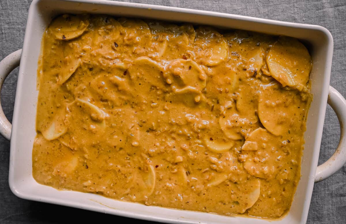 cheesy sauce spread out over potatoes for vegan scalloped potatoes