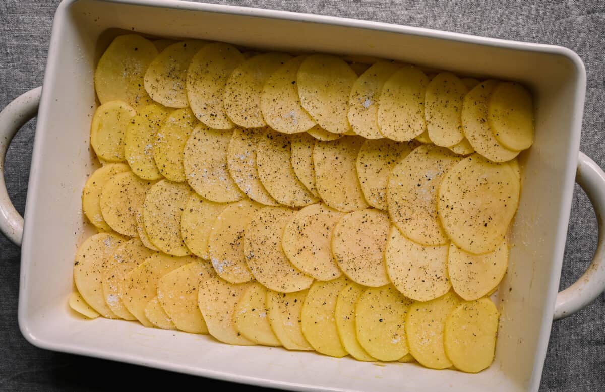 seasoned potato slices lined up in casserole pan for scalloped potatoes