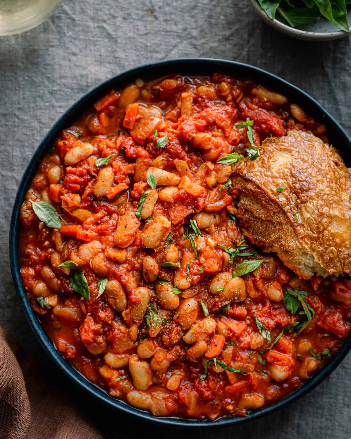 livornese stewed beans in a bowl bowl with a piece of bread on blue tablecloth