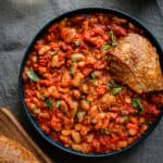 livornese stewed beans in a bowl bowl with a piece of bread on blue tablecloth.