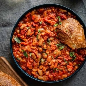 livornese stewed beans in a bowl bowl with a piece of bread on blue tablecloth.