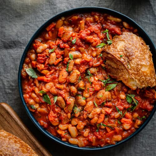 livornese stewed beans in a bowl bowl with a piece of bread on blue tablecloth