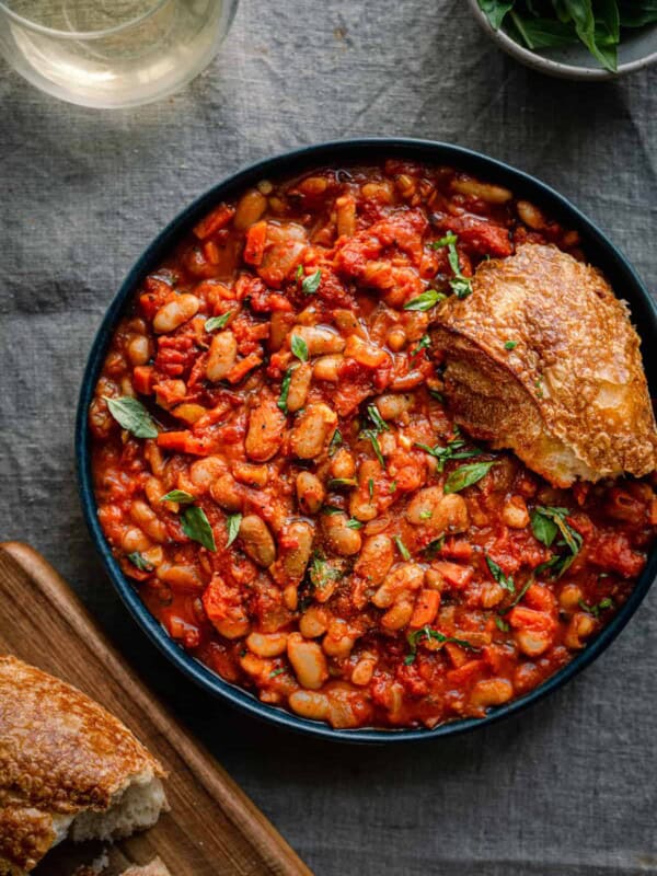 livornese stewed beans in a bowl bowl with a piece of bread on blue tablecloth.