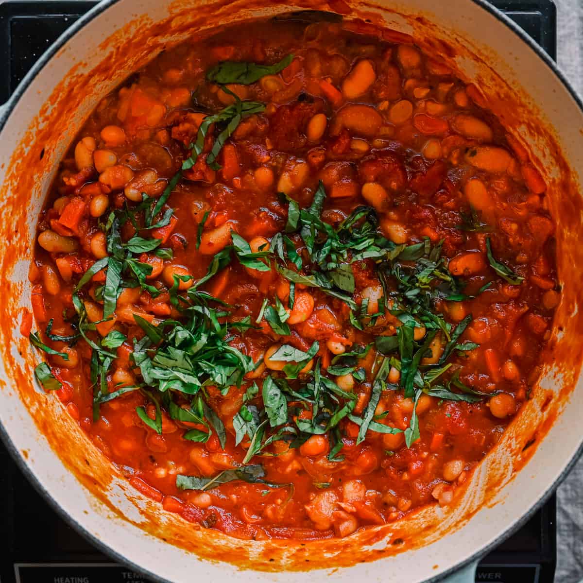 basil added to white bean tomato stew in dutch oven