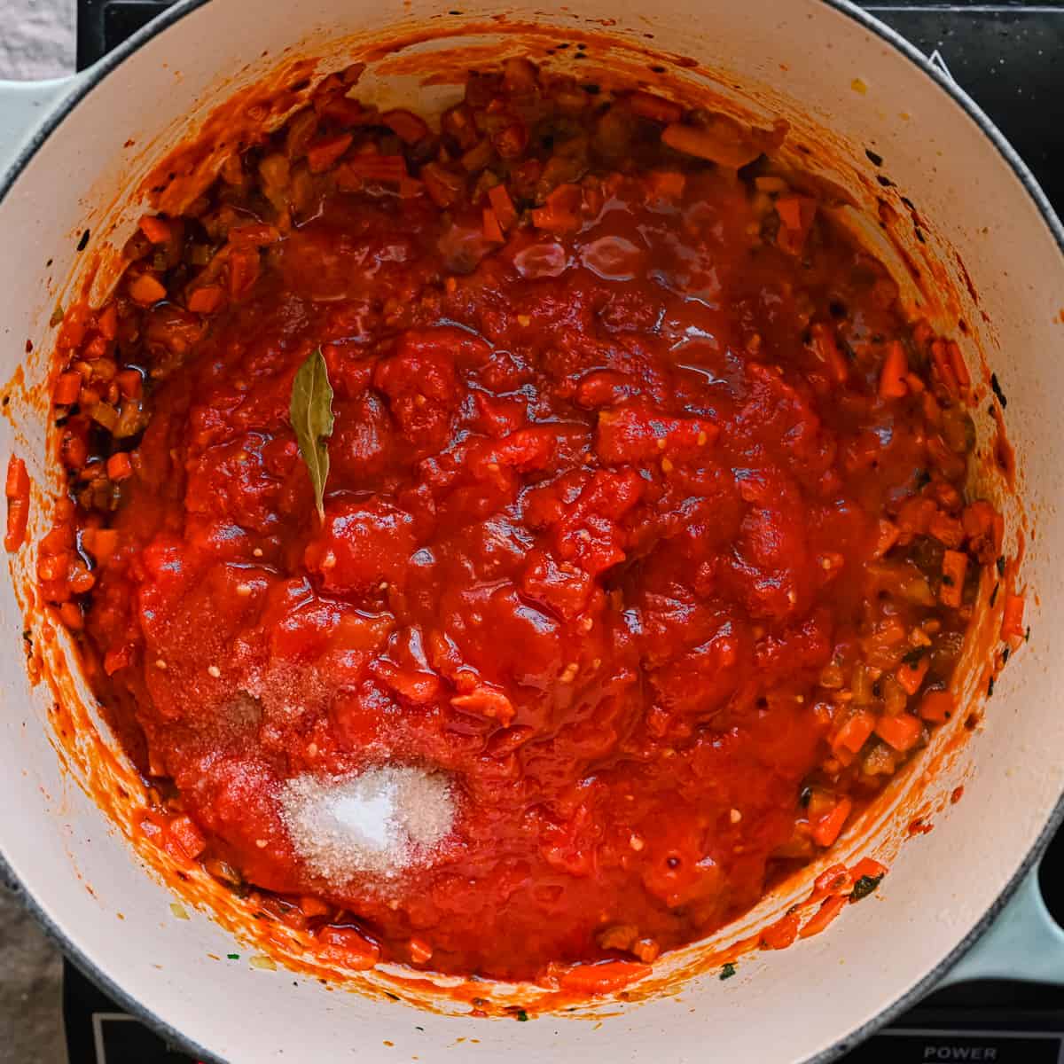 crushed tomatoes and salt sitting on top of carrots for Italian stew