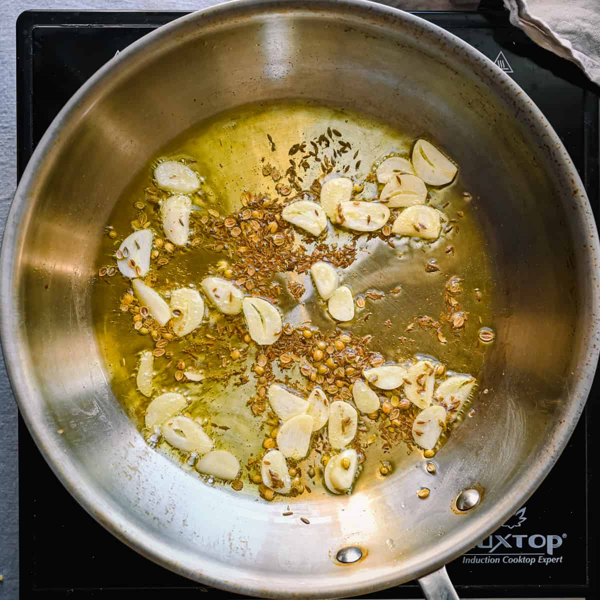 sliced garlic and cumin and coriander seeds frying in olive oil in a frying pan