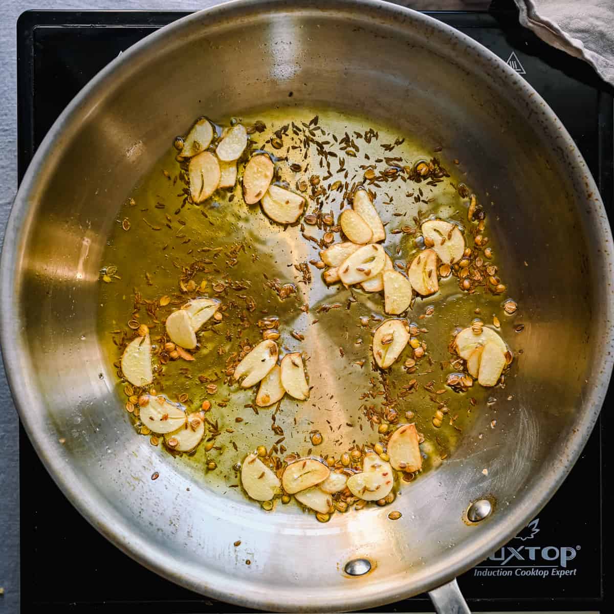 sliced garlic and cumin and coriander seeds frying in olive oil in a frying pan