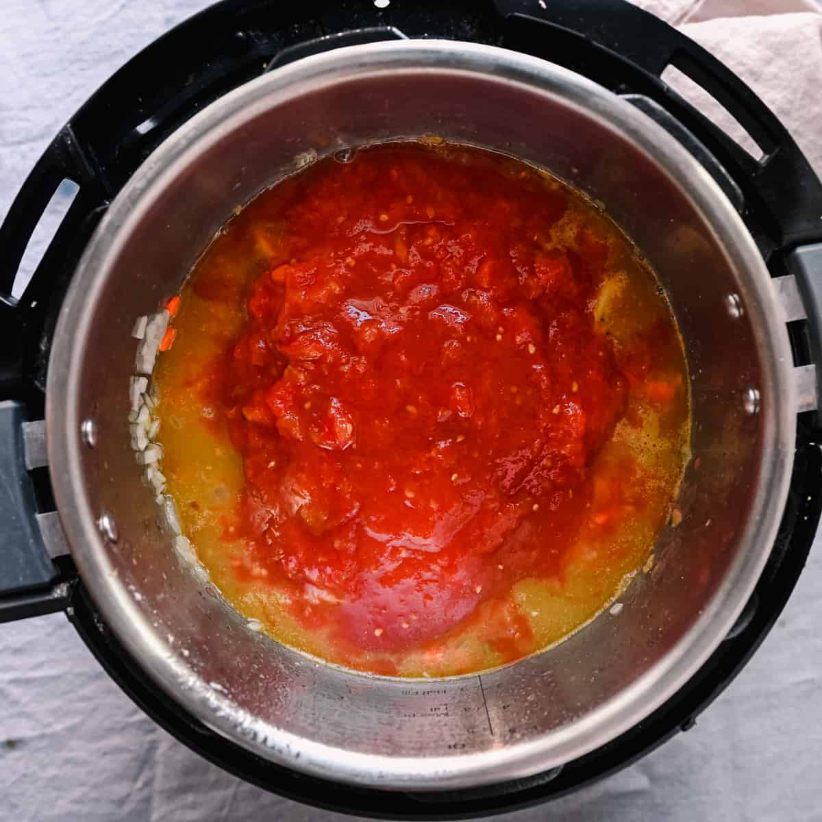 crushed tomatoes sitting on top of veggie broth in instant pot for soup