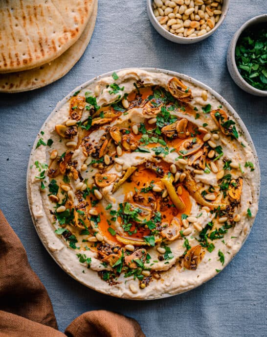 white bean dip with chili oil, garlic, parsley and pine nuts on blue tablecloth with pita bread