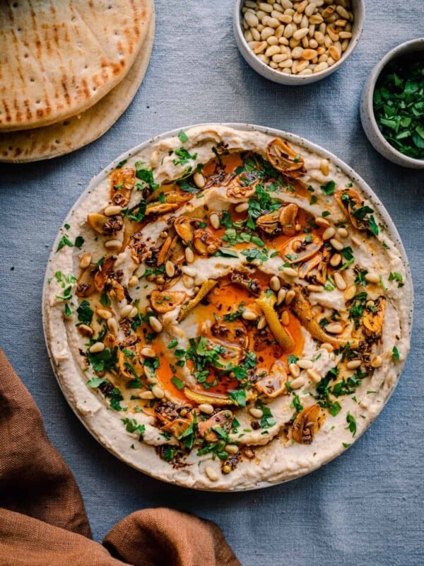 white bean dip with chili oil, garlic, parsley and pine nuts on blue tablecloth with pita bread