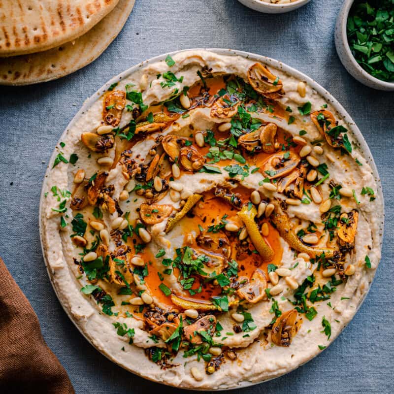 white bean dip with chili oil, garlic, parsley and pine nuts on blue tablecloth with pita bread