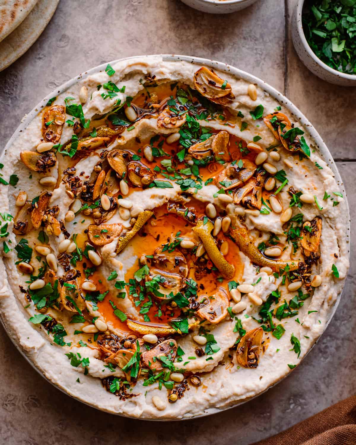 white bean dip with chili oil, garlic, parsley and pine nuts on tiled surface with pita bread