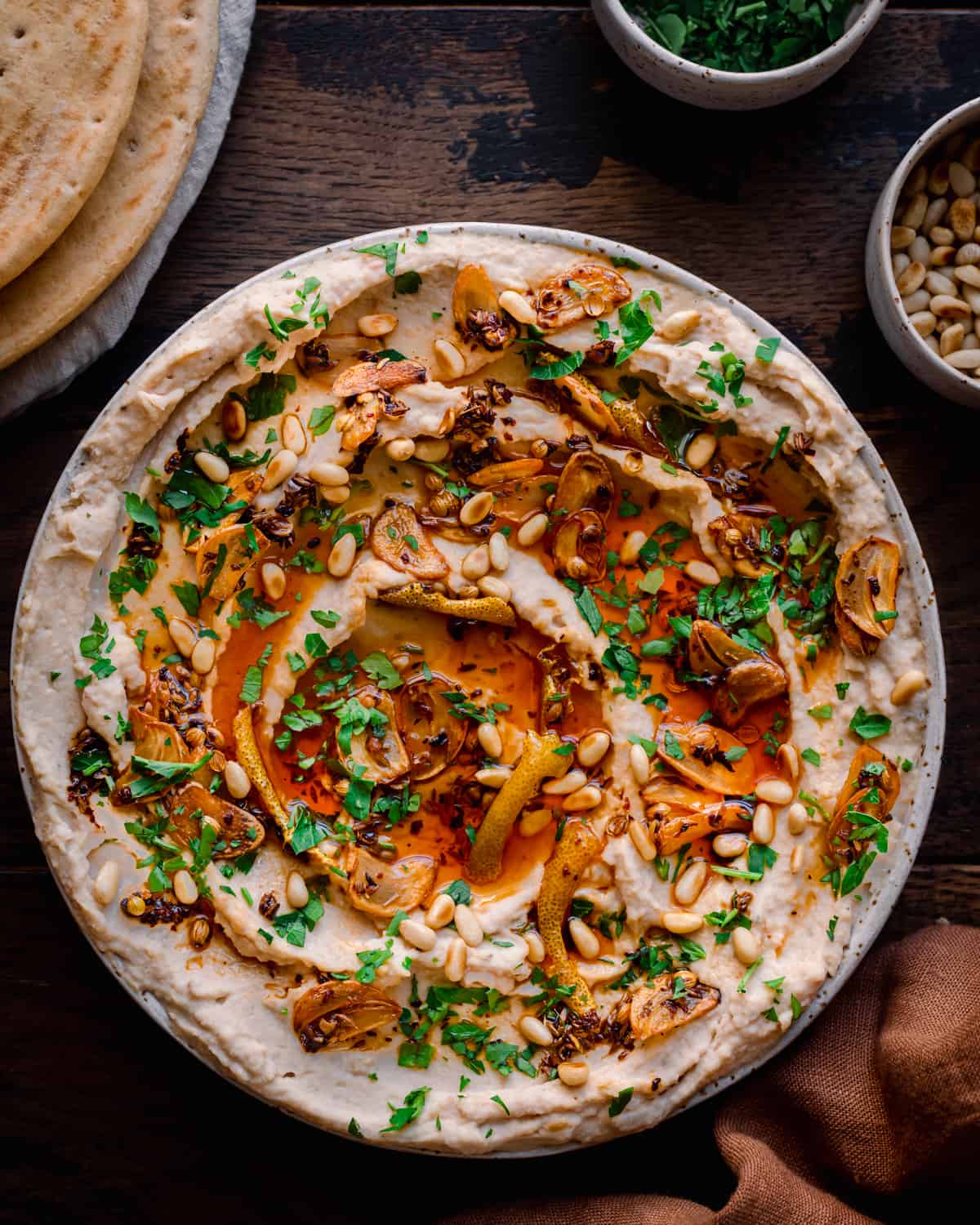 white bean dip with chili oil, garlic, parsley and pine nuts on wooden table with pita bread