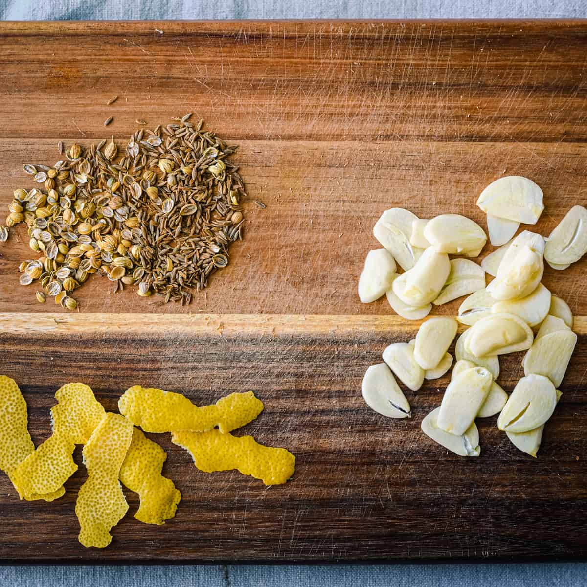 lemon peel, sliced garlic, and crushed spices on cutting board