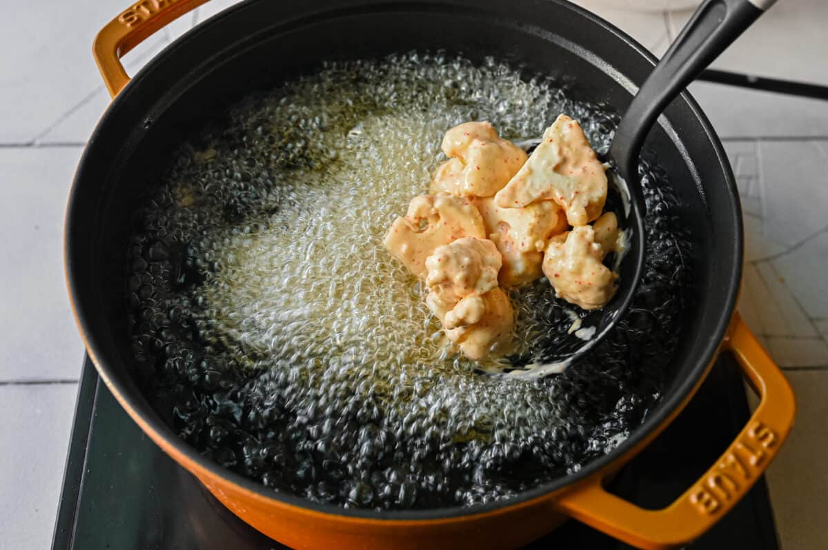 adding battered cauliflower to a pan of hot sizzling oil