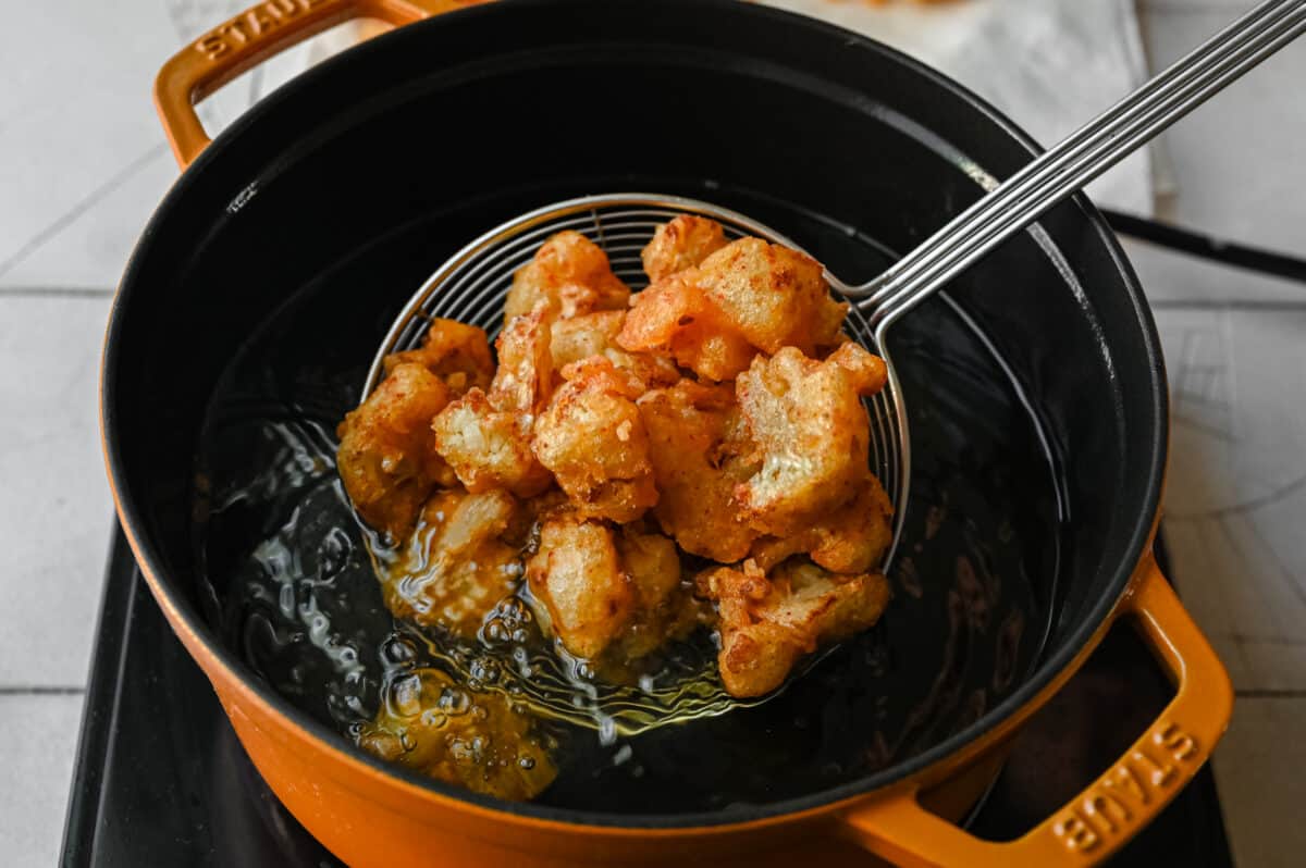 adding fried cauliflower to a pan of hot oil