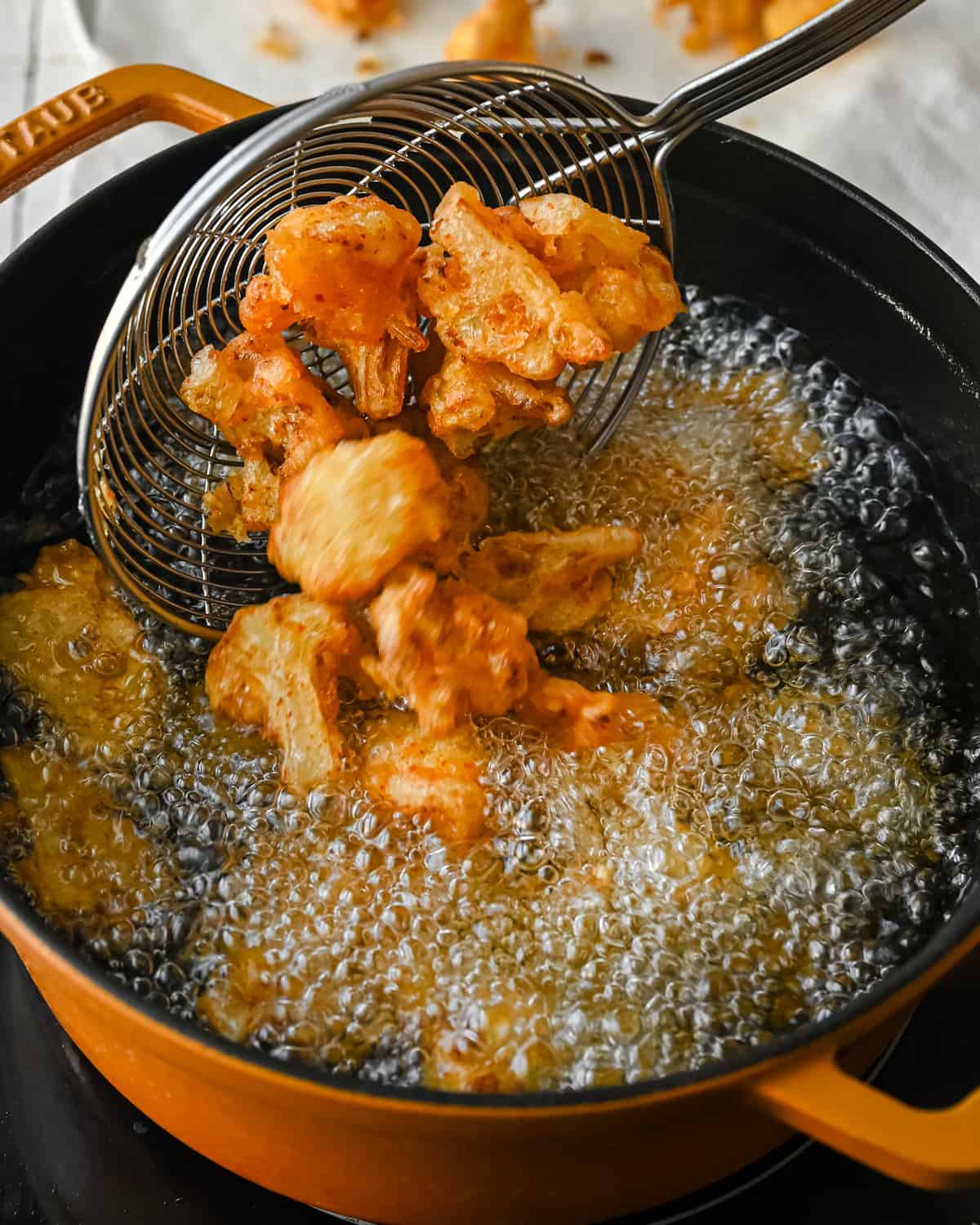 scooping fried cauliflower florets in a spider tool above a pan of hot oil