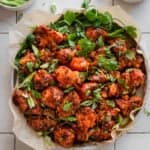 Gobi Manchurian in a parchment paper lined plate with scallions and cilantro as garnish, on white tile surface