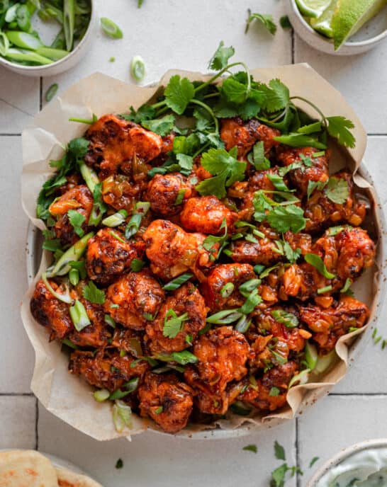 Gobi Manchurian in a parchment paper lined plate with scallions and cilantro as garnish, on white tile surface