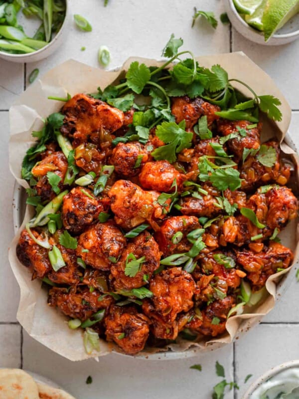 Gobi Manchurian in a parchment paper lined plate with scallions and cilantro as garnish, on white tile surface