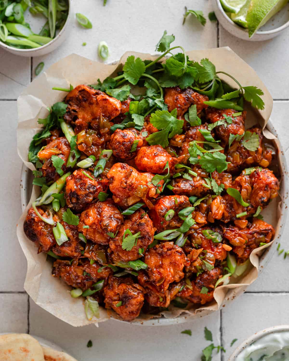 Gobi Manchurian in a parchment paper lined plate with scallions and cilantro as garnish, on white tile surface