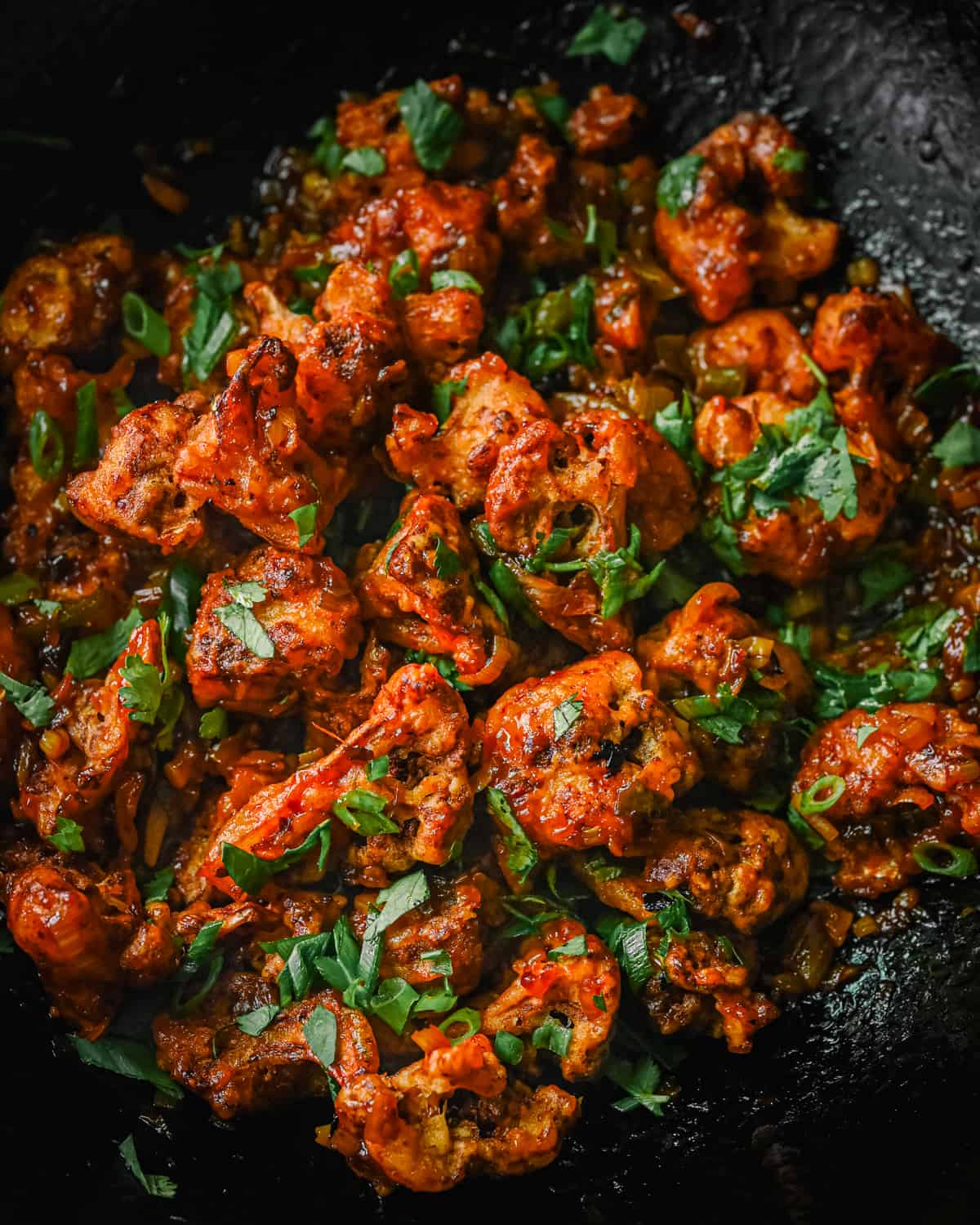 Gobi Manchurian in a wok, garnished with scallions and cilantro