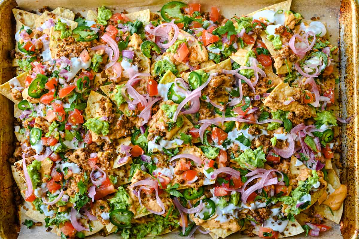 tray of vegan nachos with guacamole, queso, pickled onoins, jalapenos, and taco meat
