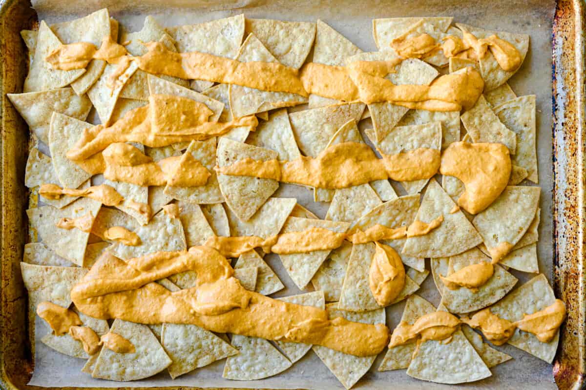 tortilla chips on lined sheet pan with vegan queso drizzled on top