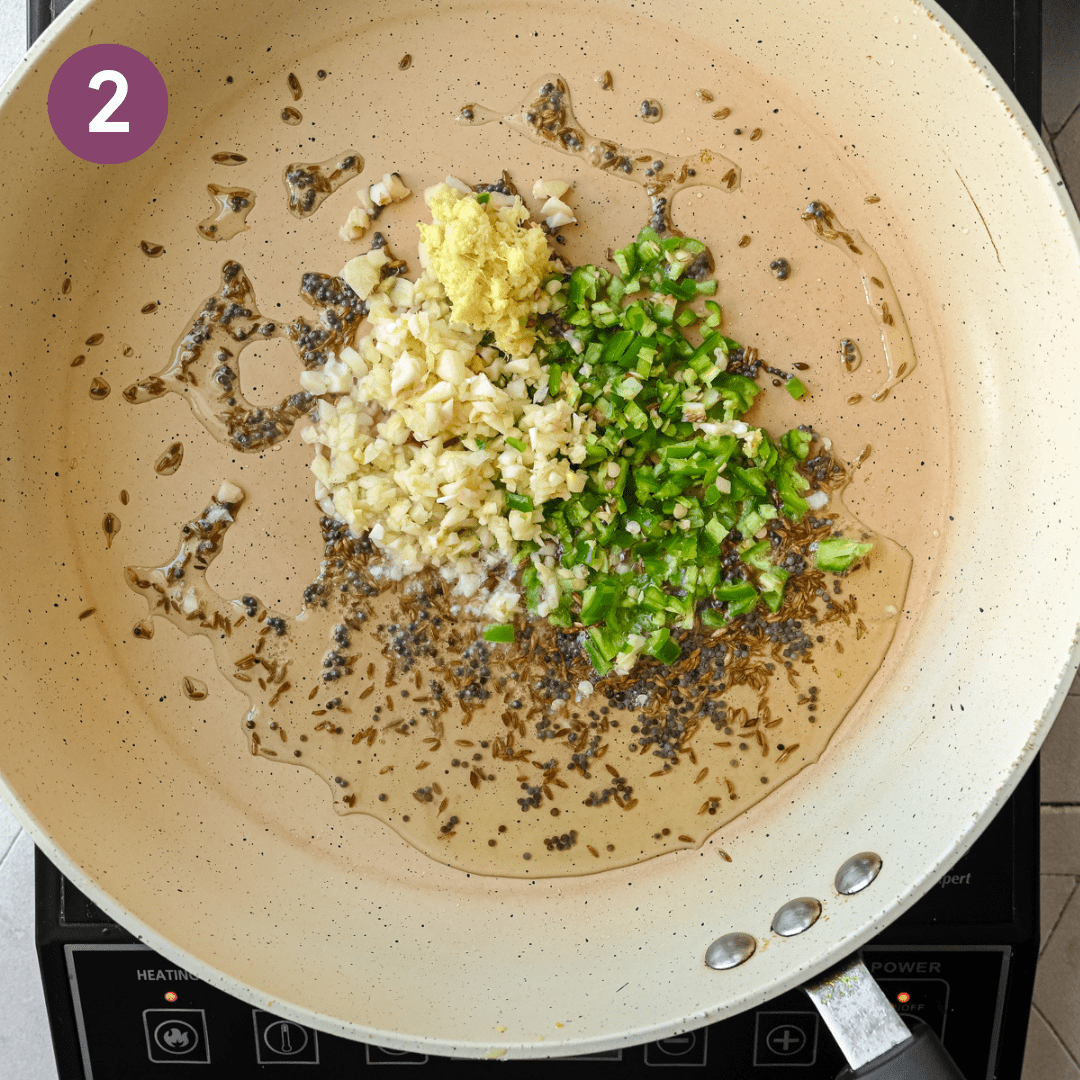 garlic, ginger, and green chile peppers withmustard seeds and cumin seeds frying in oil in a frying pan.