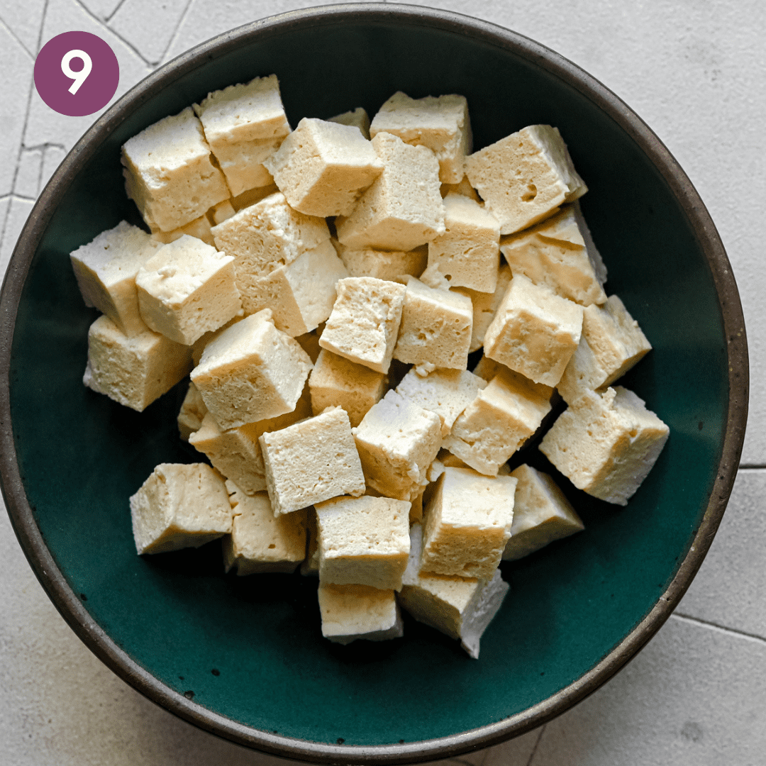 chewy cubes of tofu that have been boiled sitting in a green bowl.
