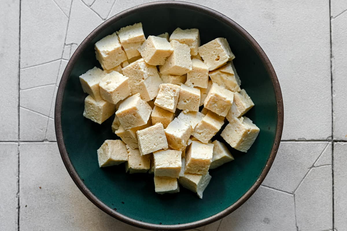 defrosted and boiled tofu cubes in a green bowl.