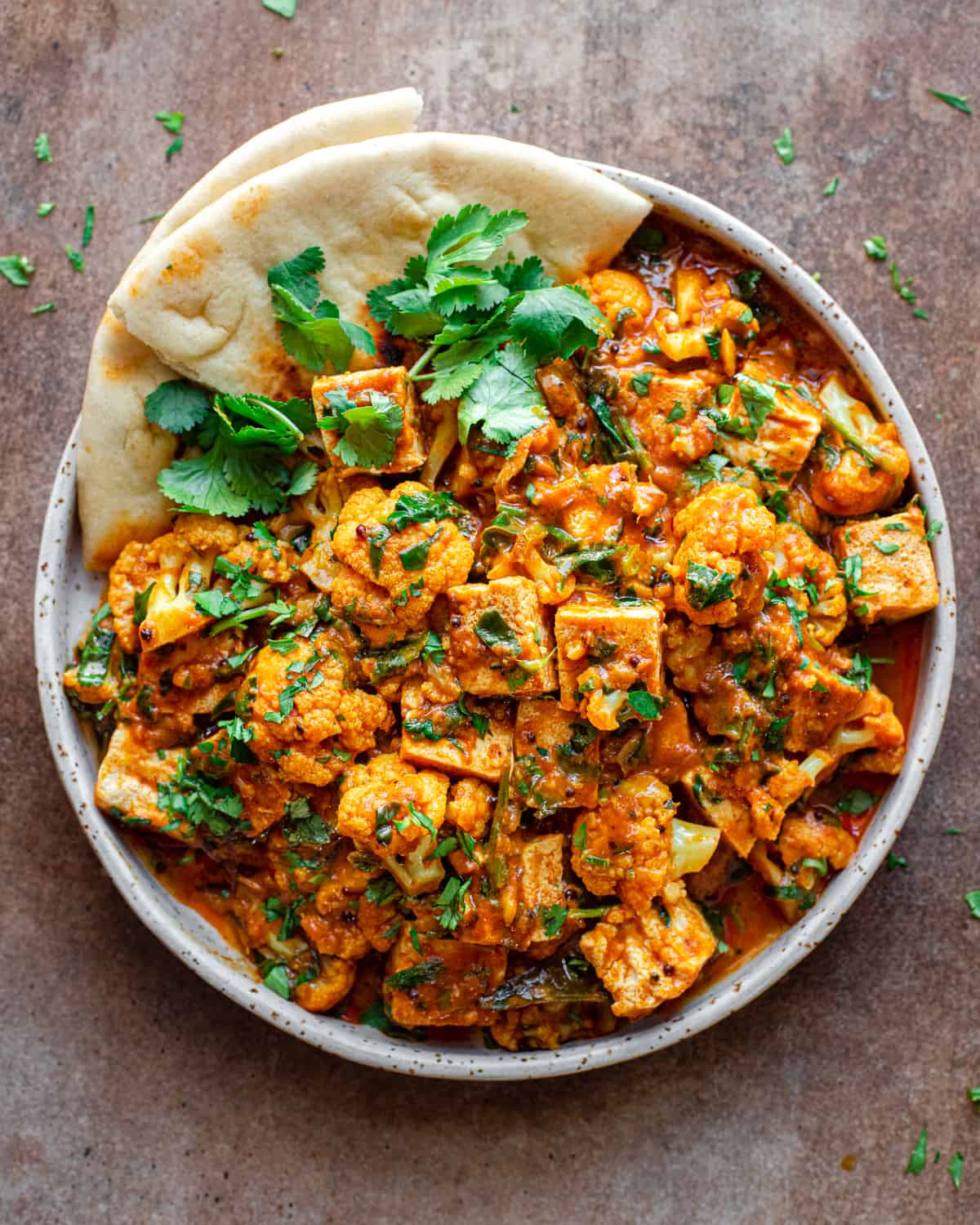 vegan curry with tofu in a white plate with naan and cilantro on brown surface