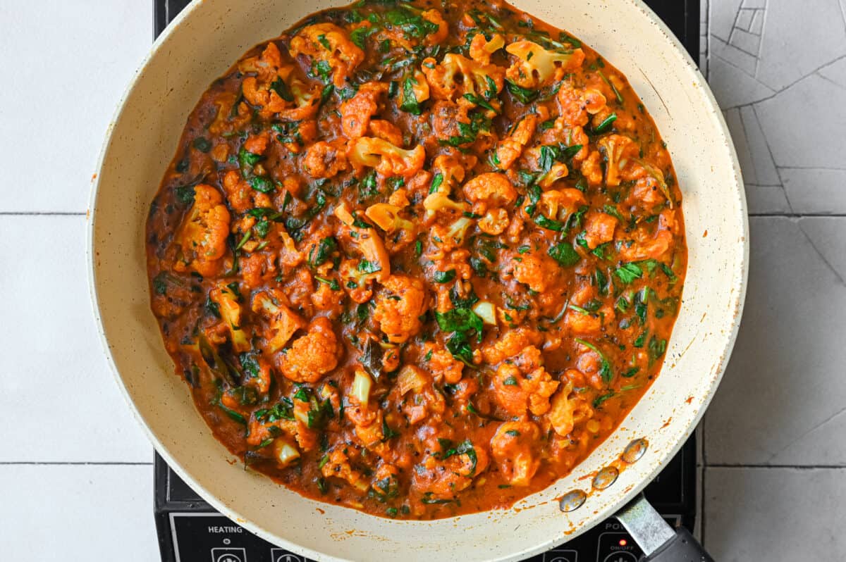 Indian vegan curry with cauliflower and spinach in a frying pan