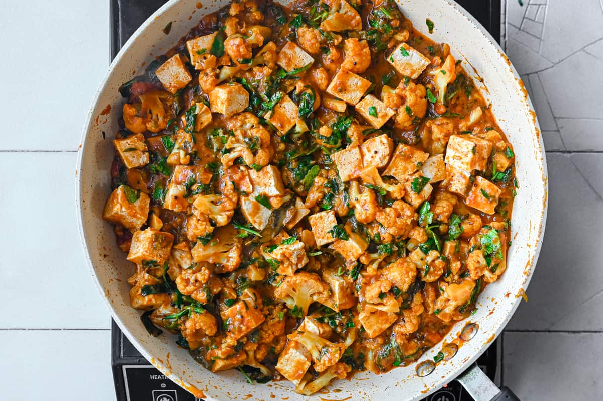Indian spiced vegan curry with tofu and cauliflower in a frying pan.