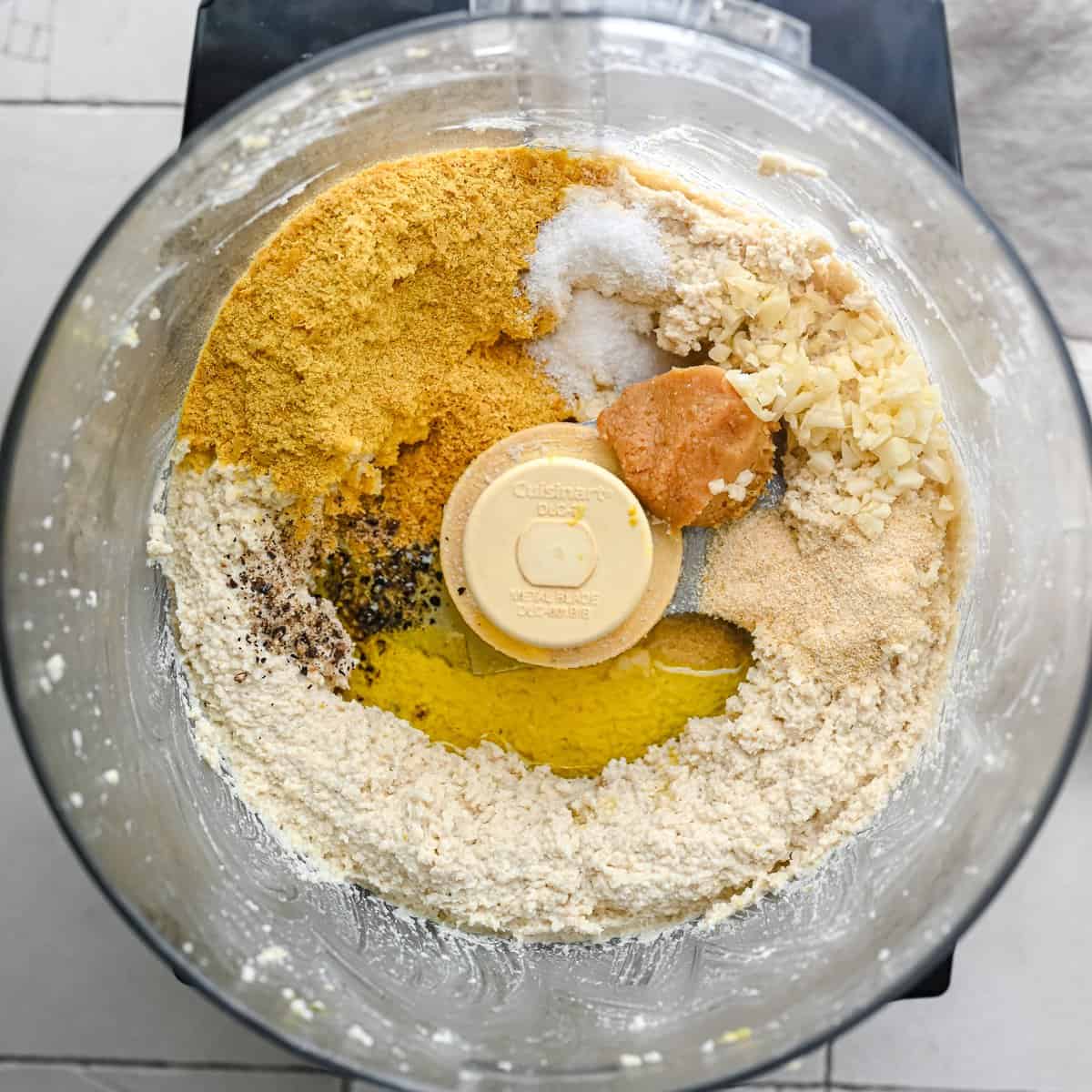 blended vegan ricotta made of cashews in food processor bowl with nutritional yeast, seasonings, and olive oil