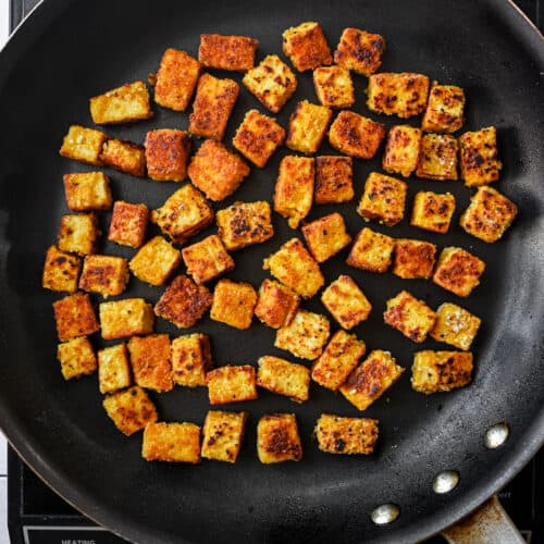 golden brown pan-fried tofu cubes in a black skillet